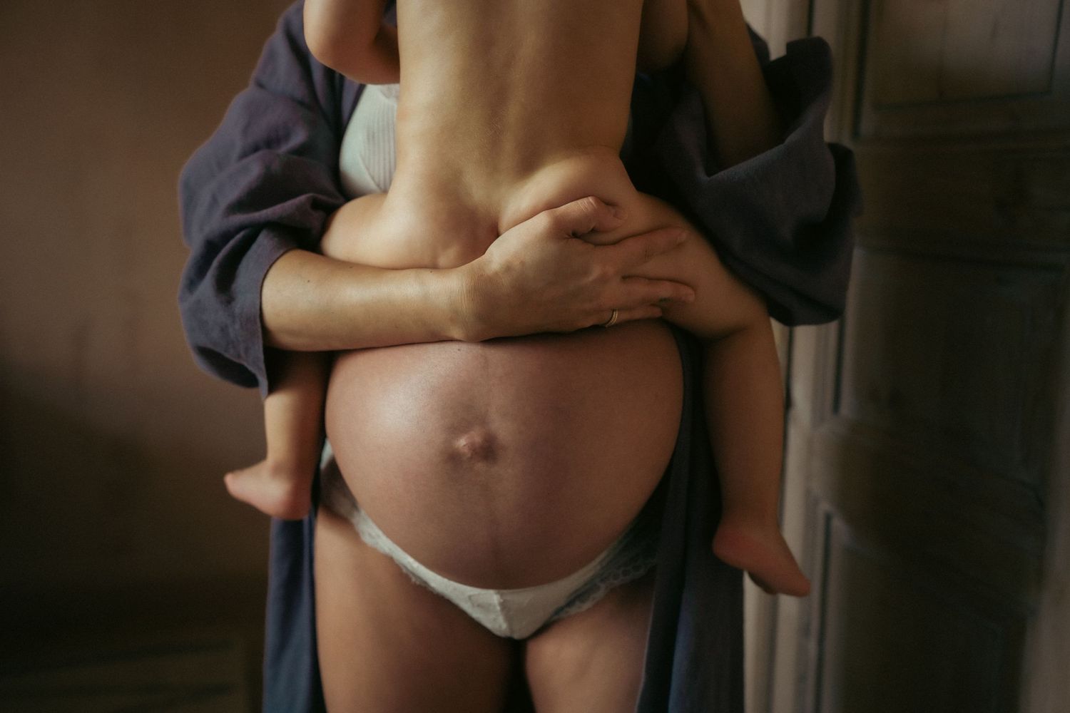 peuter zit op de bolle buik van zijn mama die bijna is uitgerekend van haar tweede zoontje