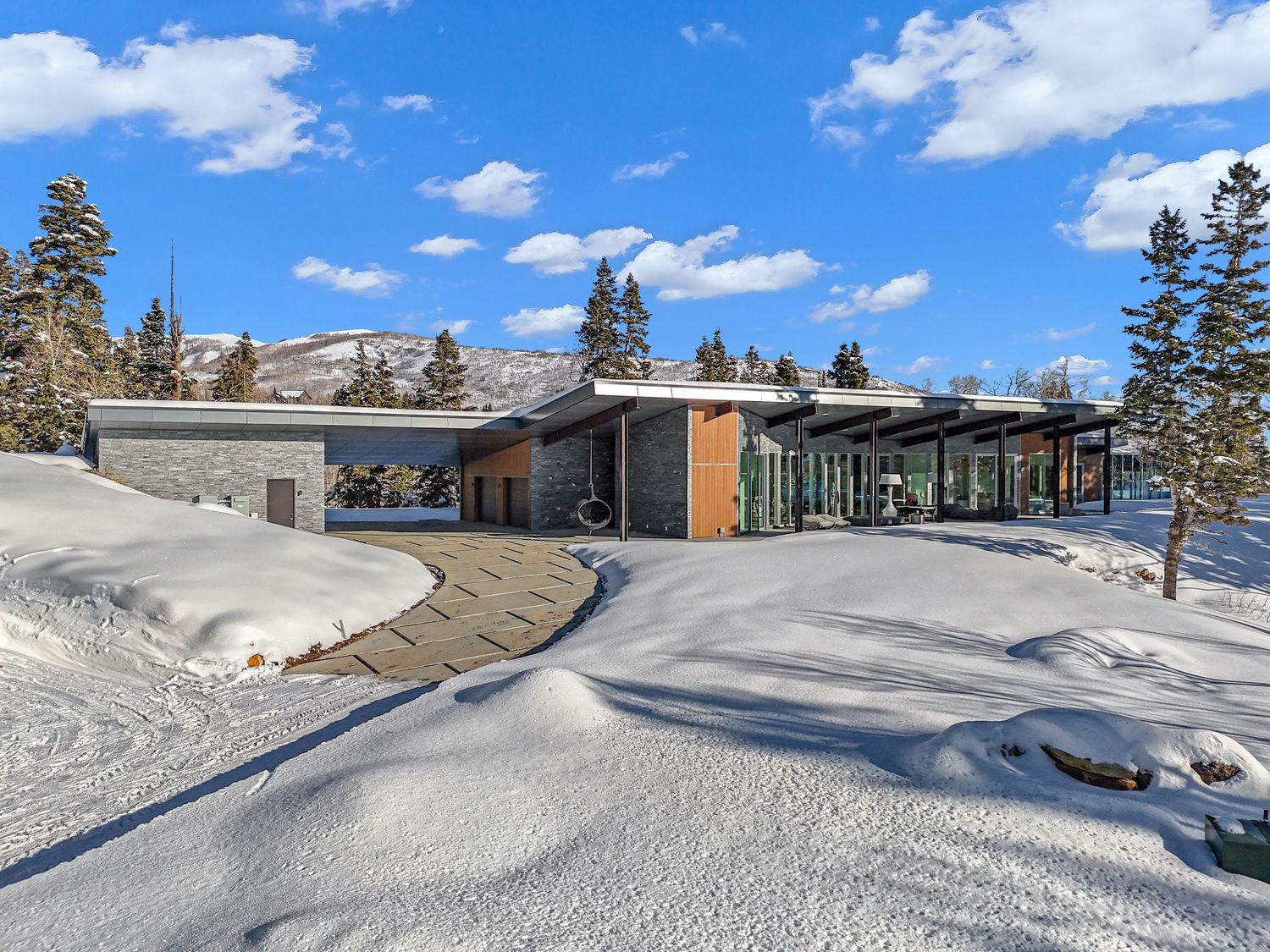 Contemporary luxury home exterior surrounded by snow-covered landscape with mountain views and trees. Captured by Slate Media (best in UT)