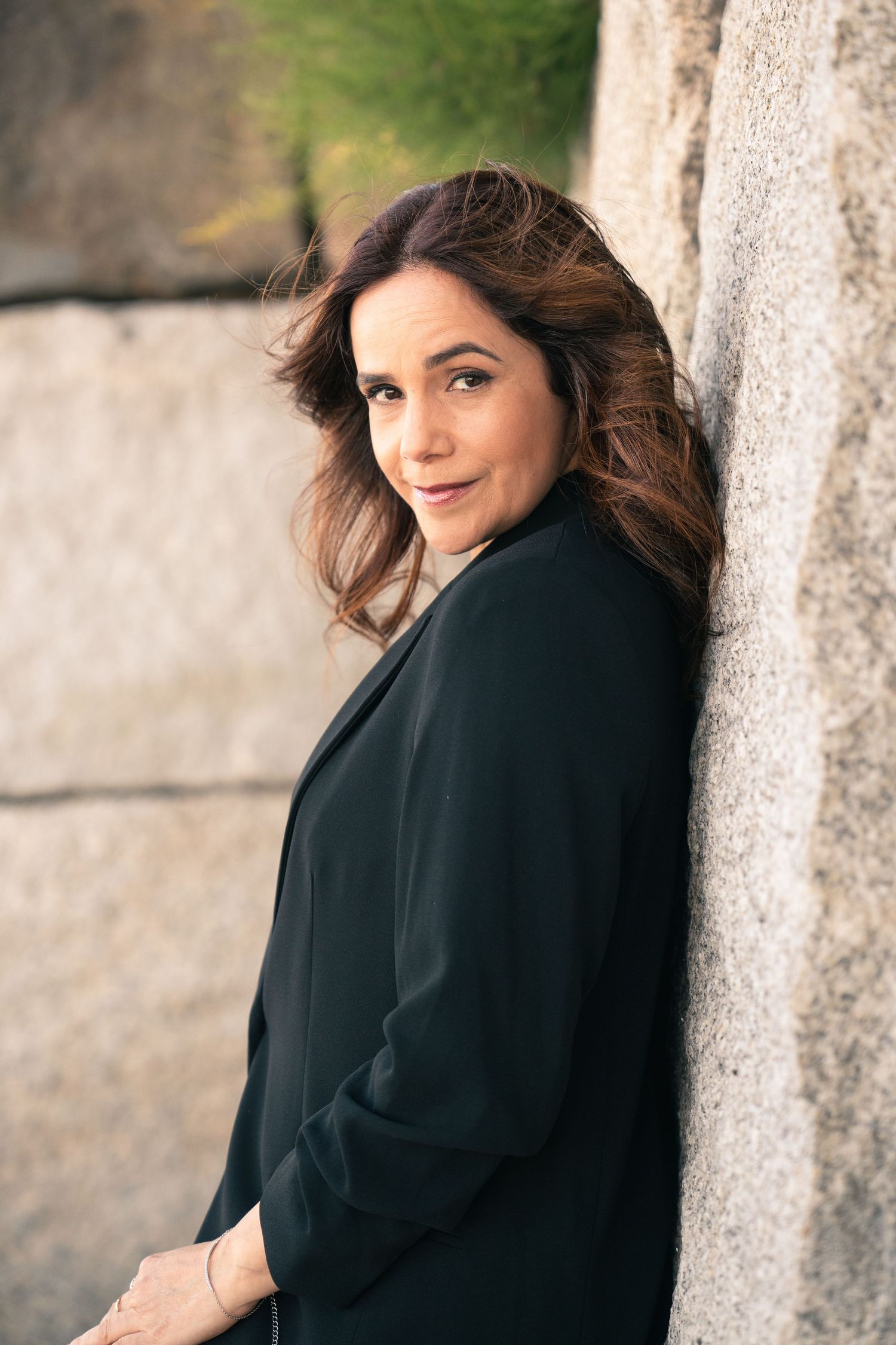Woman in black jacket posing against stone column in dramatic portrait series.