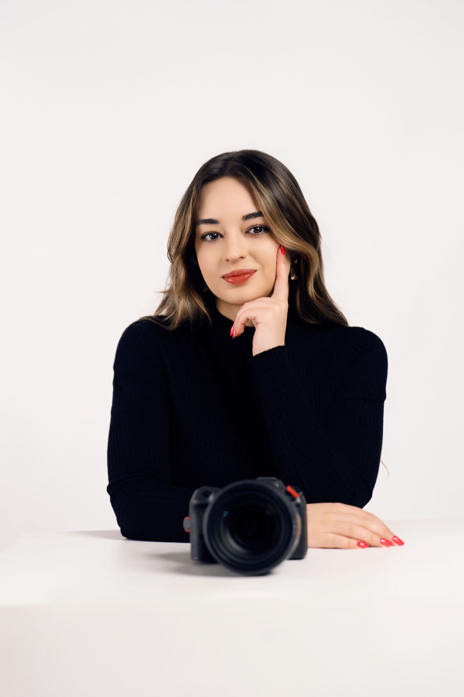 Professional photographer in black turtleneck posing with camera on white background.