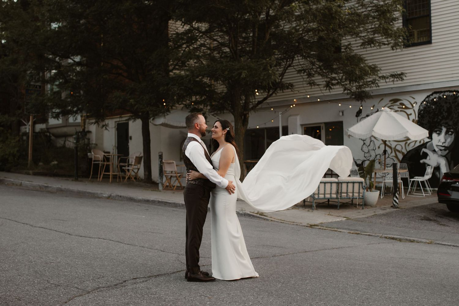 A couple embraces on a quiet street as the bride's dress billows in the wind.