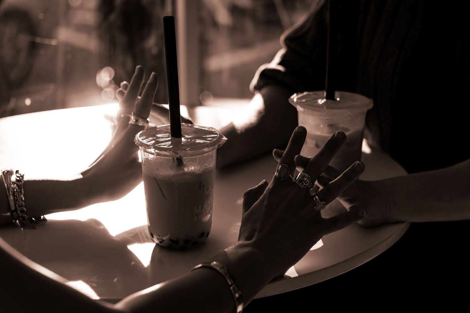 A sapphic couple links hands in an Ashland boba shop. They're wearing rings and bracelets, photographed in black and white.