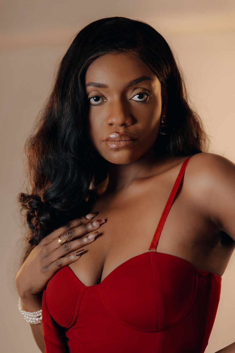 close shot of a female model in a beautiful red dress with goldeing lighting and hand on chest pose