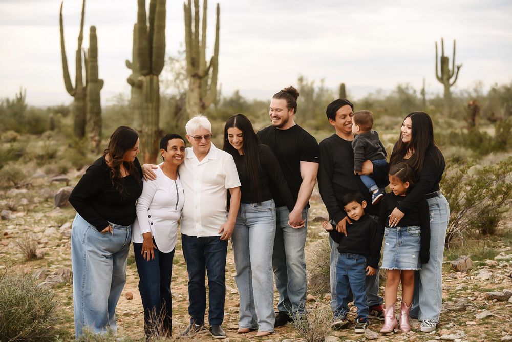 Multi-generational family poses outdoors in Arizona desert with saguaro cacti, wearing casual black tops and jeans.