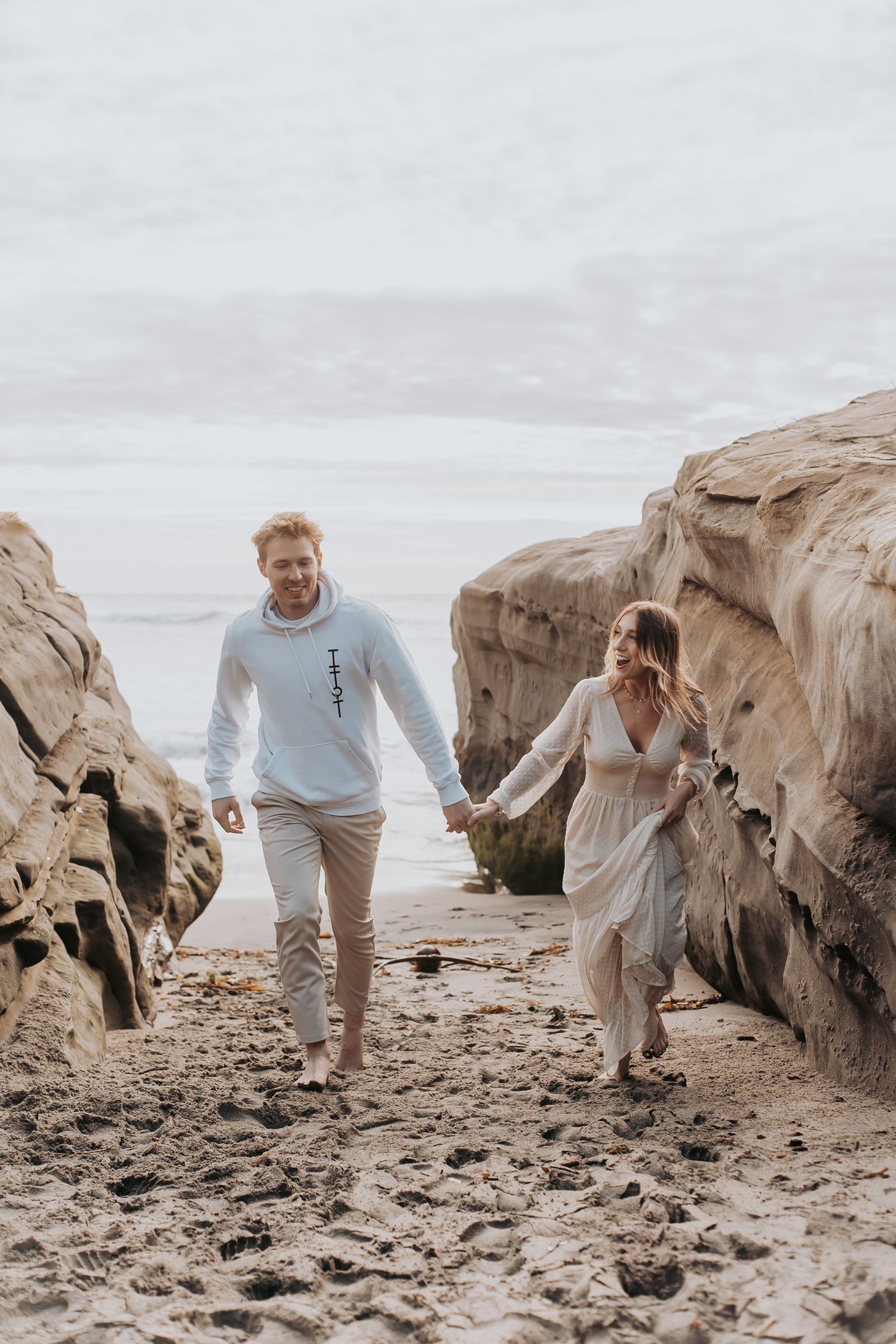 Couple walking hand in hand through rocky beach pathway.