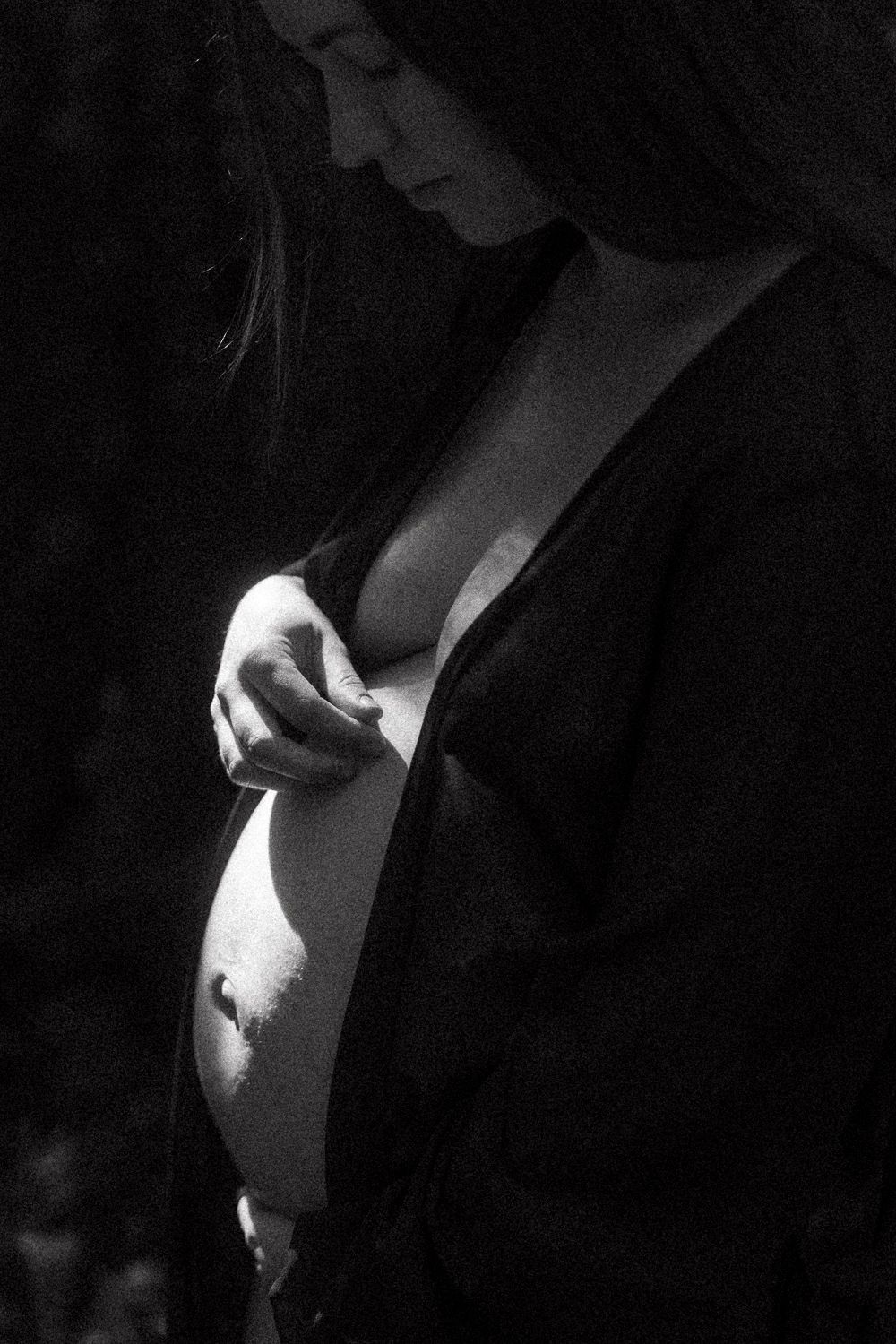 A moody black and white portrait series showing dramatic contrasts of light and shadow on expecting mothers.