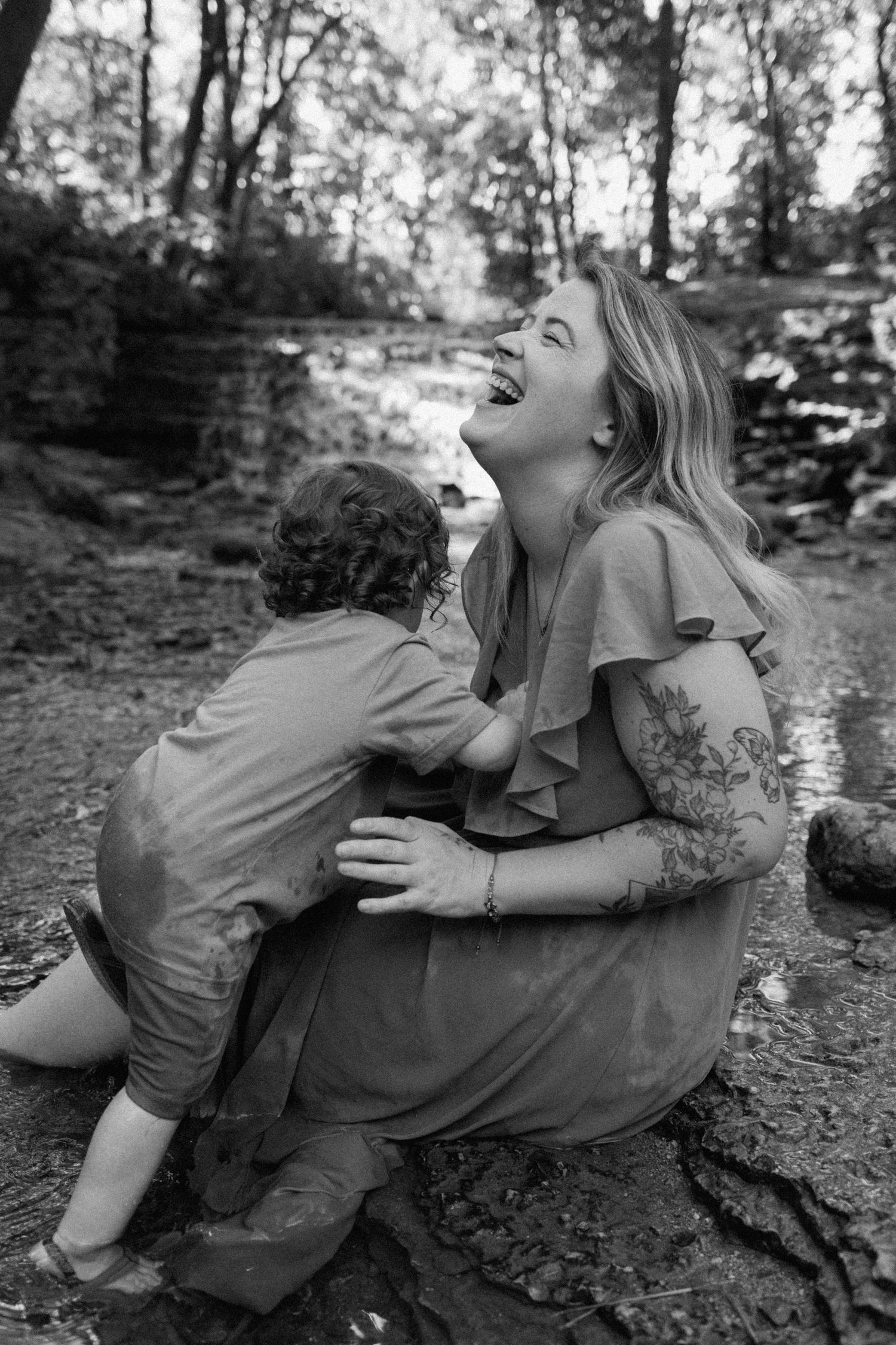 Black and white candid photograph showing a joyful moment shared between parent and toddler outdoors in nature.
