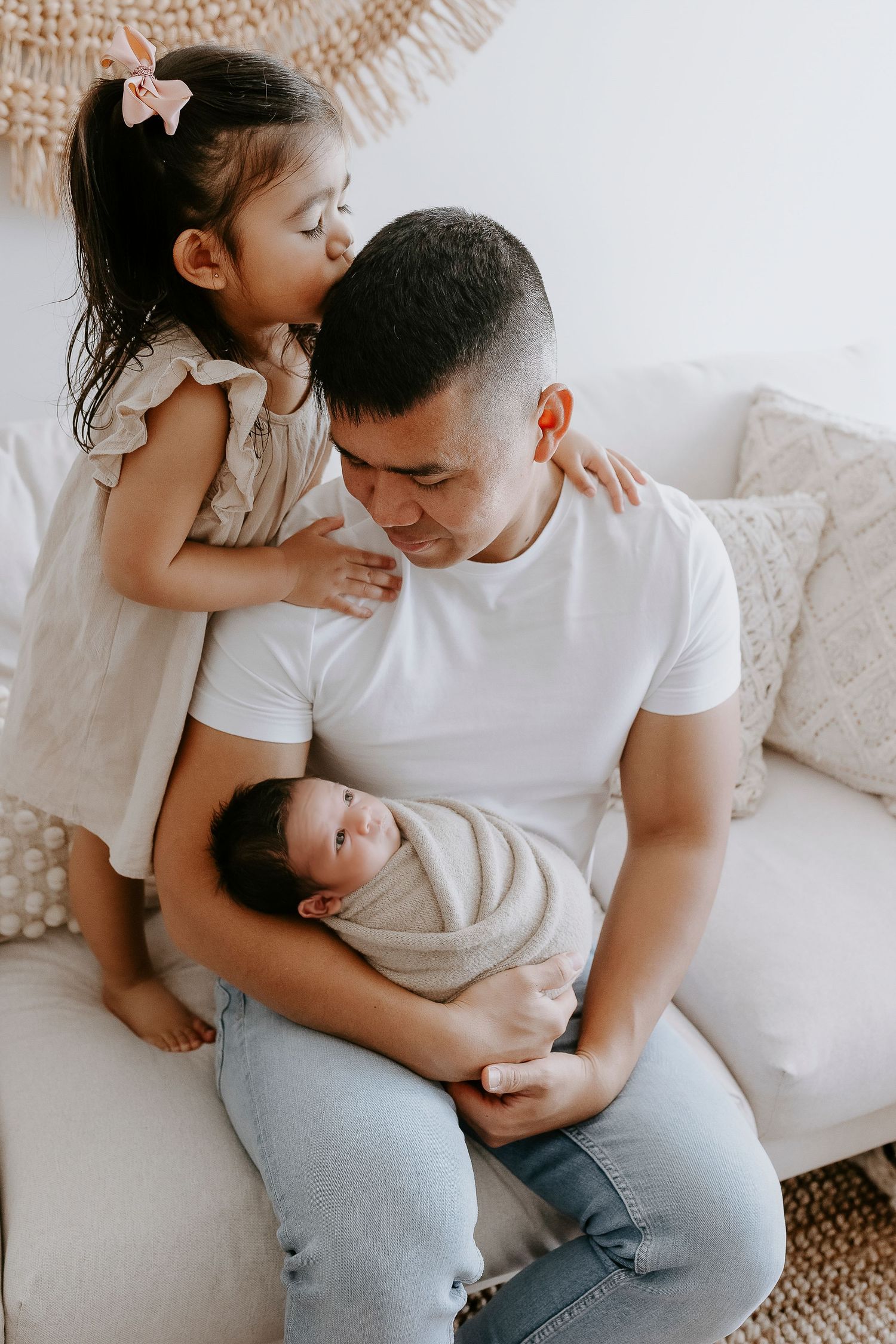 Sweet family moment on white couch with baby and child in soft natural lighting.