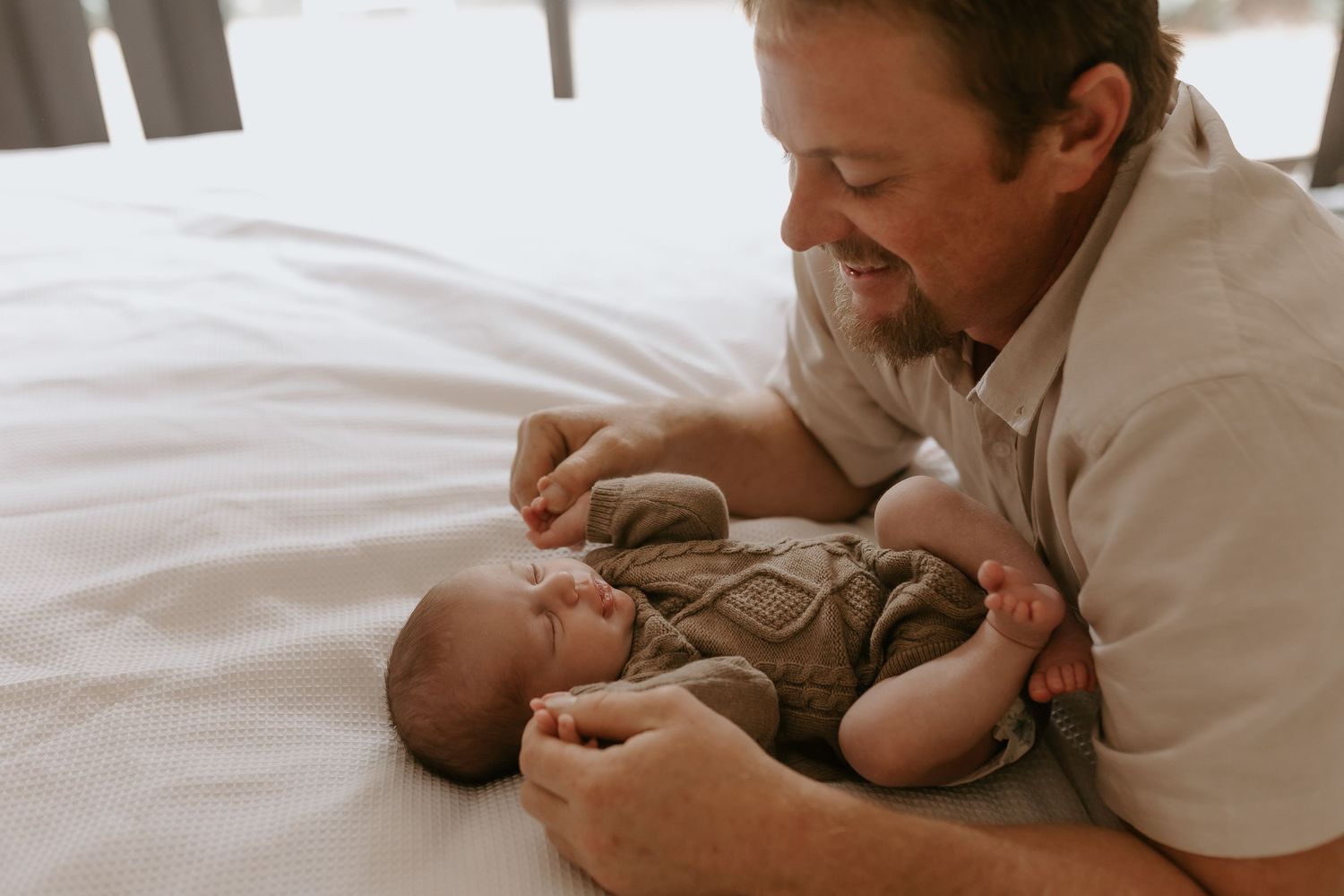 A sweet bonding moment between parent and baby lying on white bedding.
