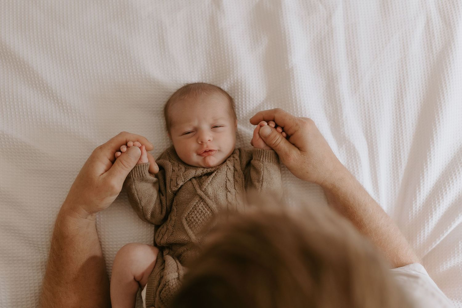A sleeping baby in gray clothing with hands gently touching their face.