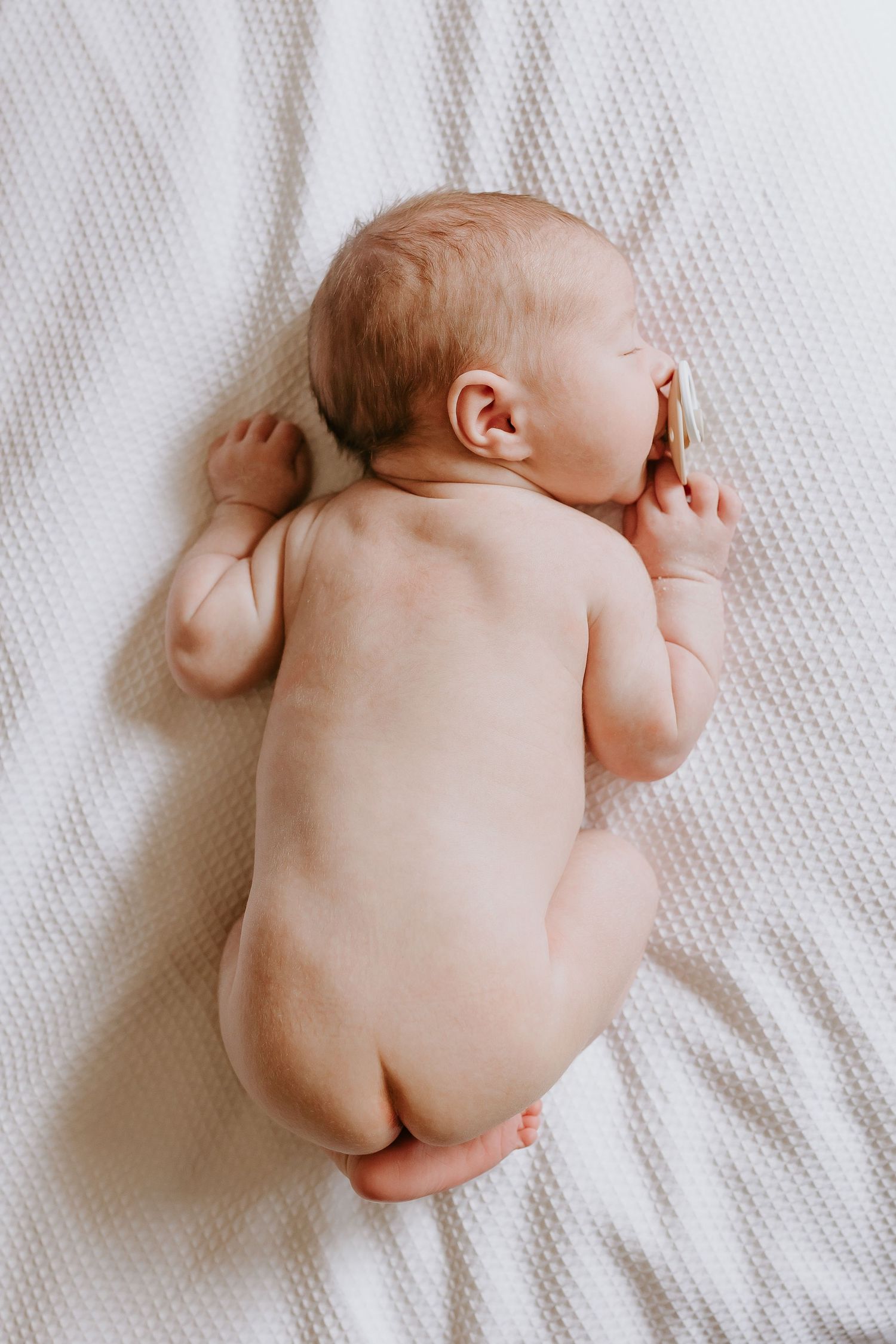 A newborn baby sleeping peacefully on white textured bedding.