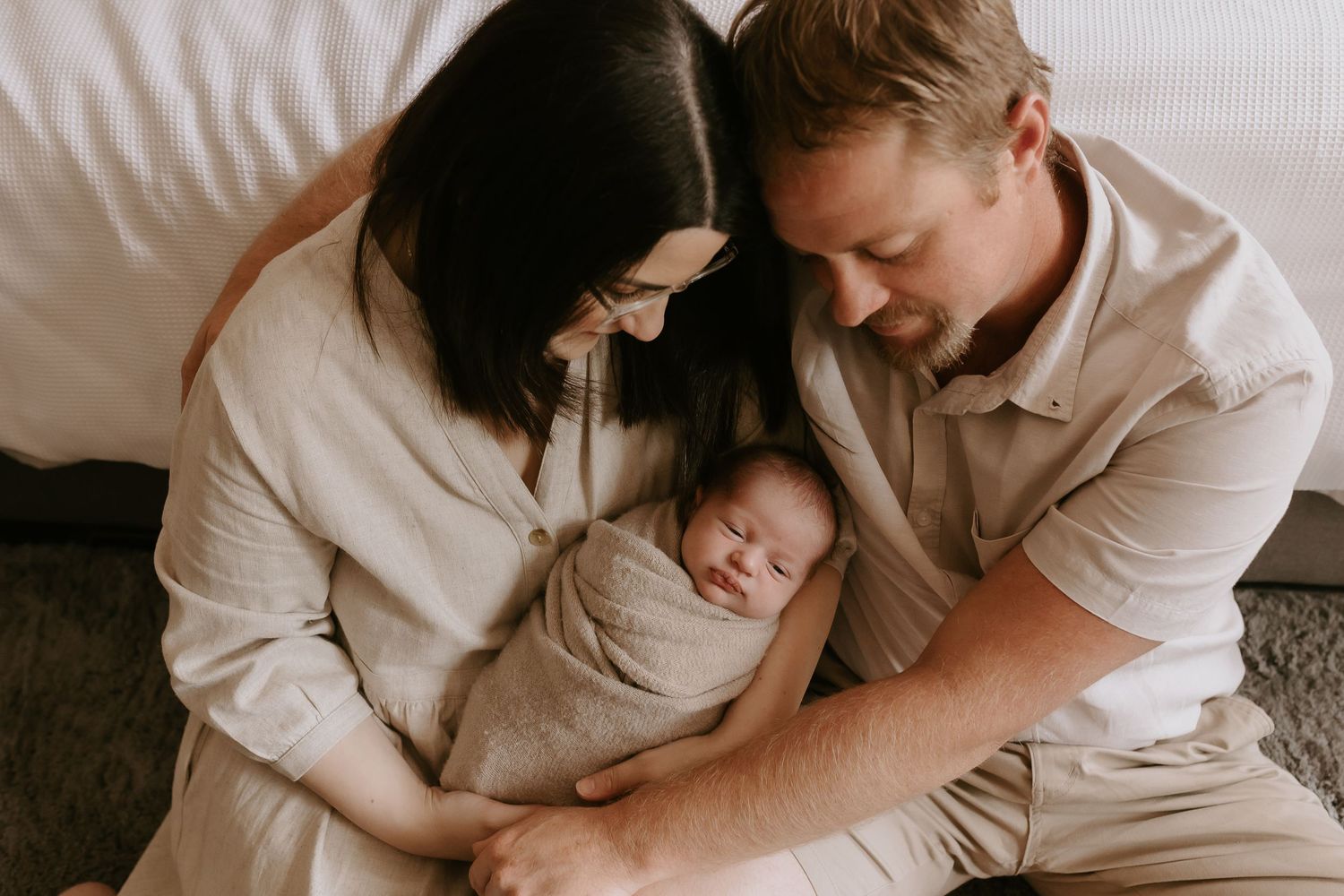 An intimate family portrait with parents cradling their sleeping newborn.