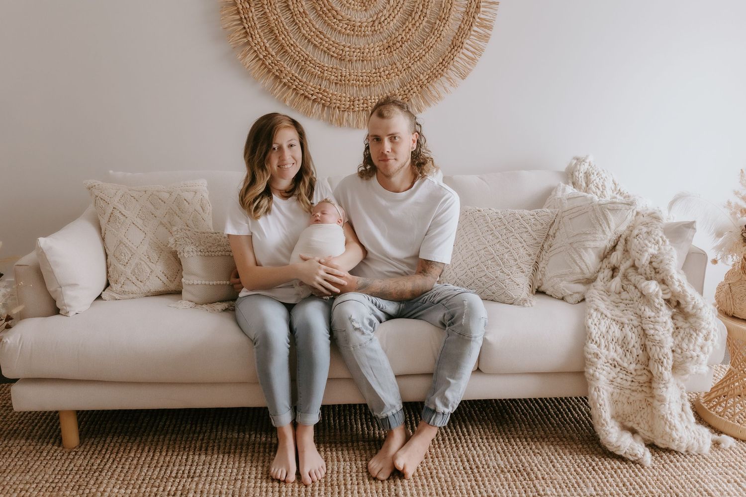 Couple sits together on beige couch beneath circular woven wall hanging.
