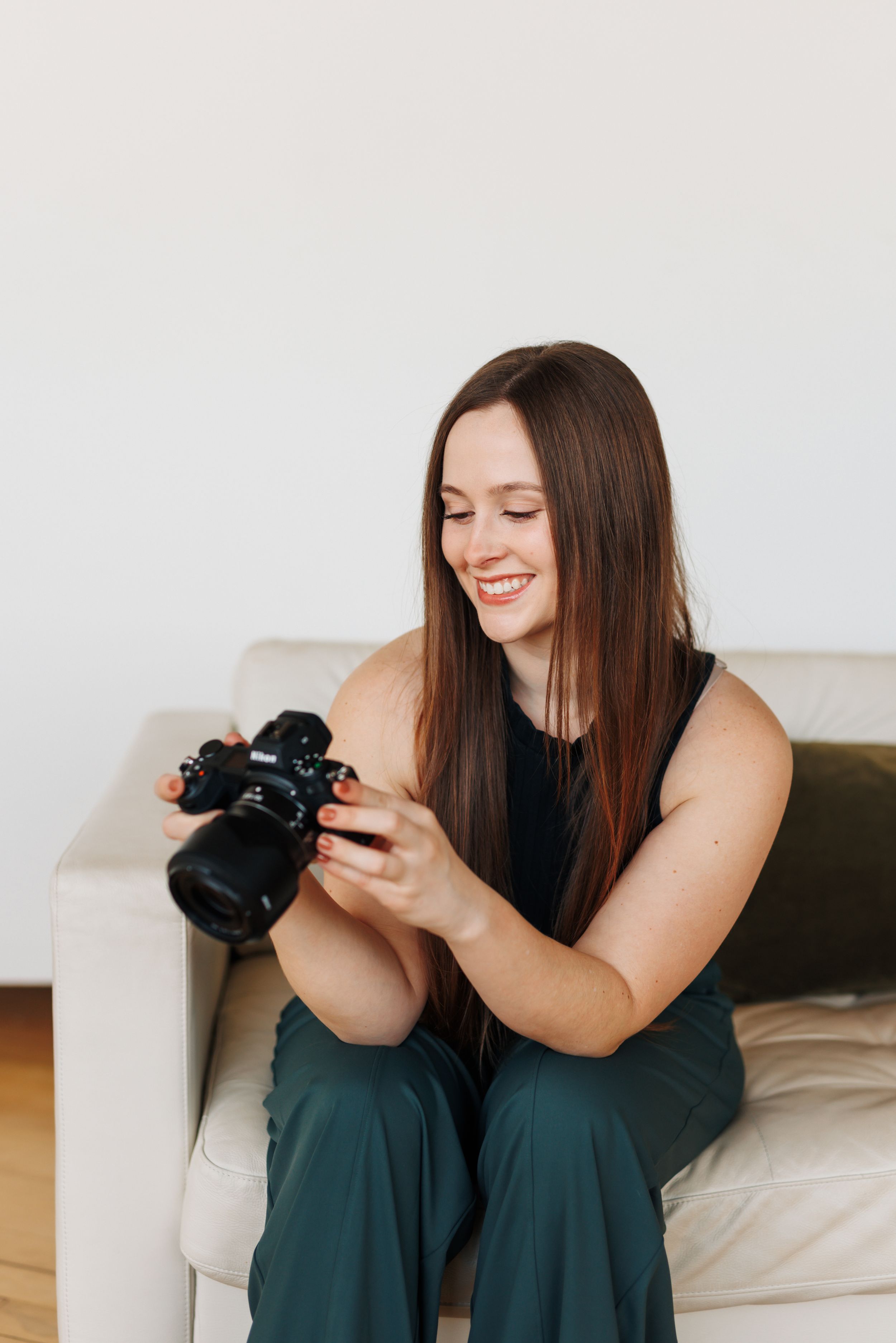Photographer checks images on mirrorless camera while relaxing on white couch.