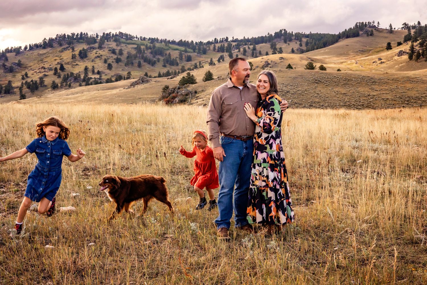 A family plays along a grassy hillside during autumn with colorful red maple trees in the background.