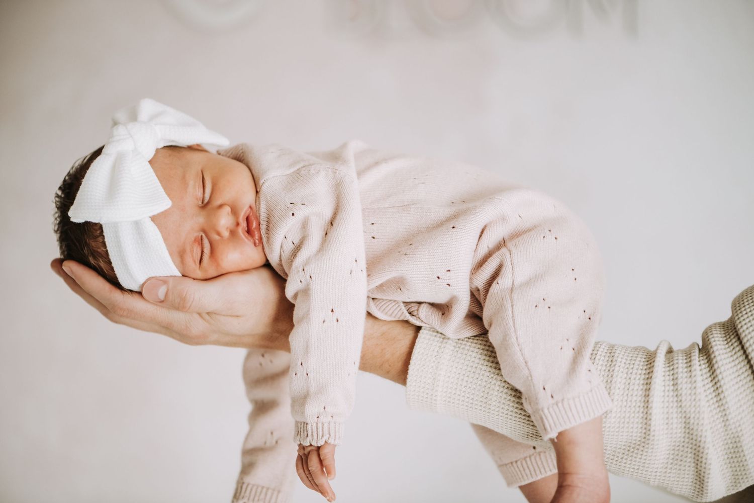 Sleeping baby in cream outfit against light background. highlighting candid, storytelling, lifestyle natural light newborn photography