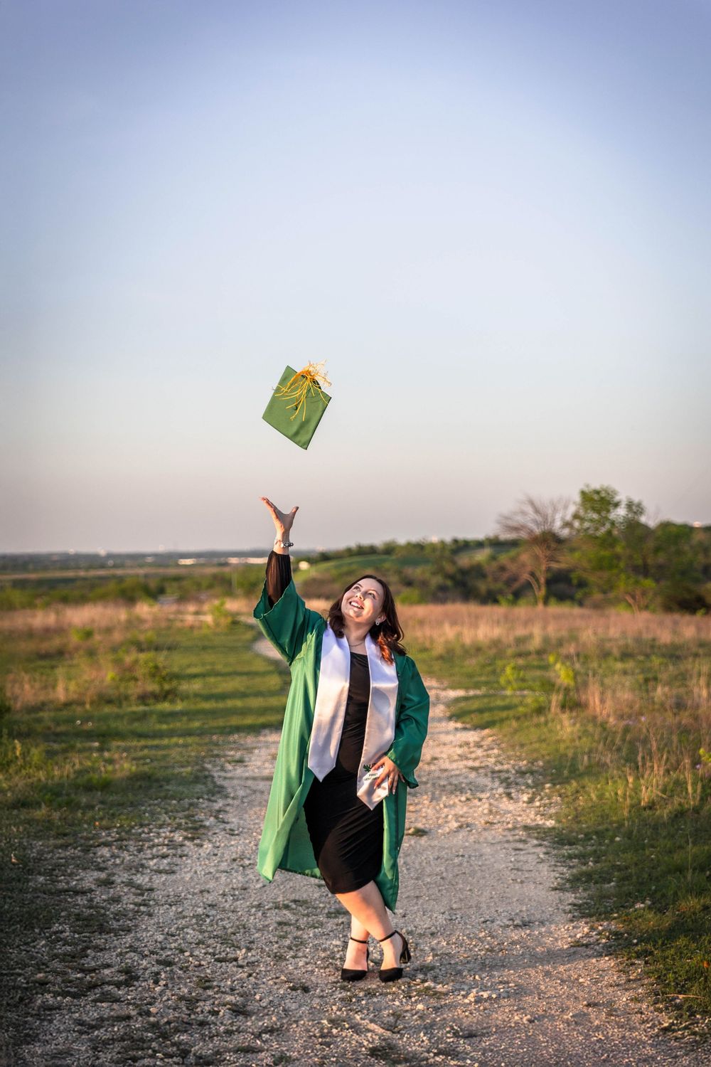 A senior girl in her cap and gown throws her cap into the air in a field.