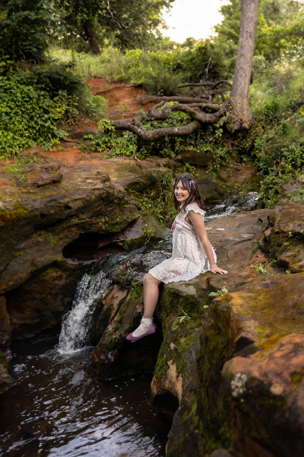 A young girl poses with a waterfall.