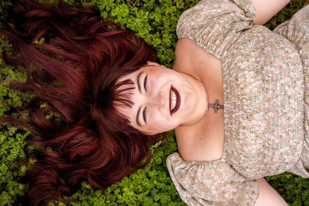 A beautiful woman with red hair lays in clovers.