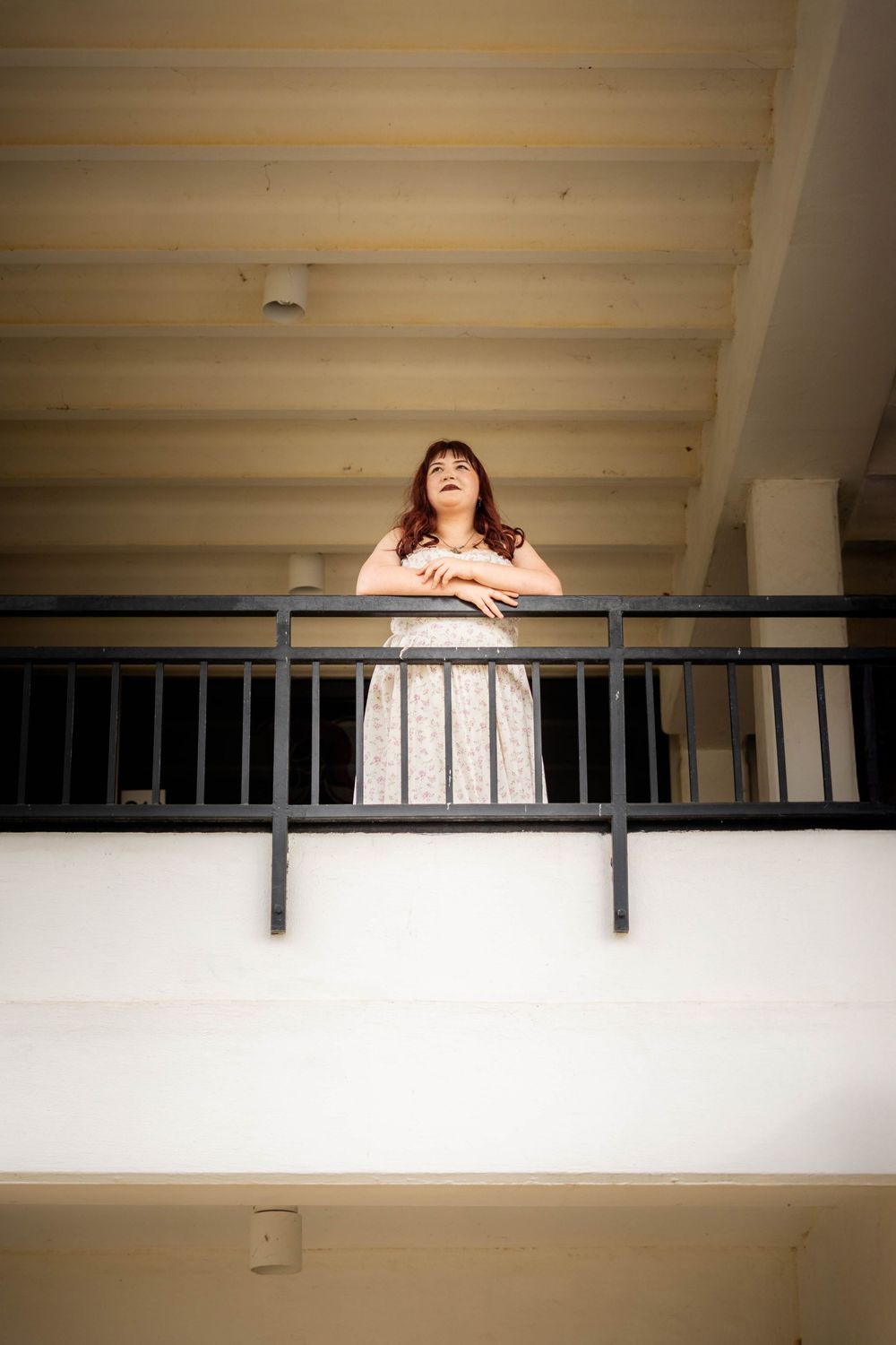 A young woman poses on a balcony behind the railing.