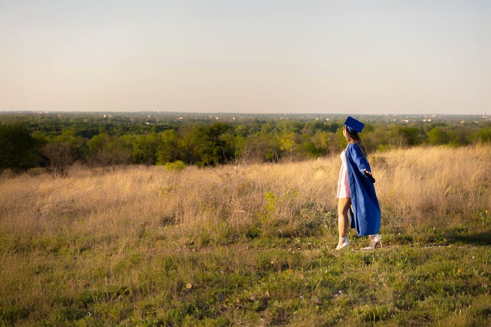 A senior in a cap and gown walks through a beautiful field.
