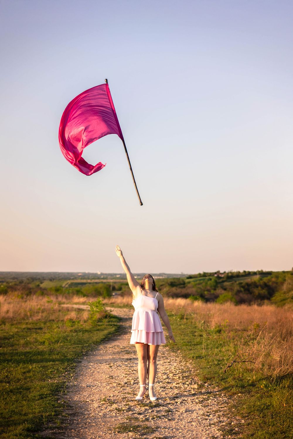A senior girl throws her color guard flag into the air in a field.
