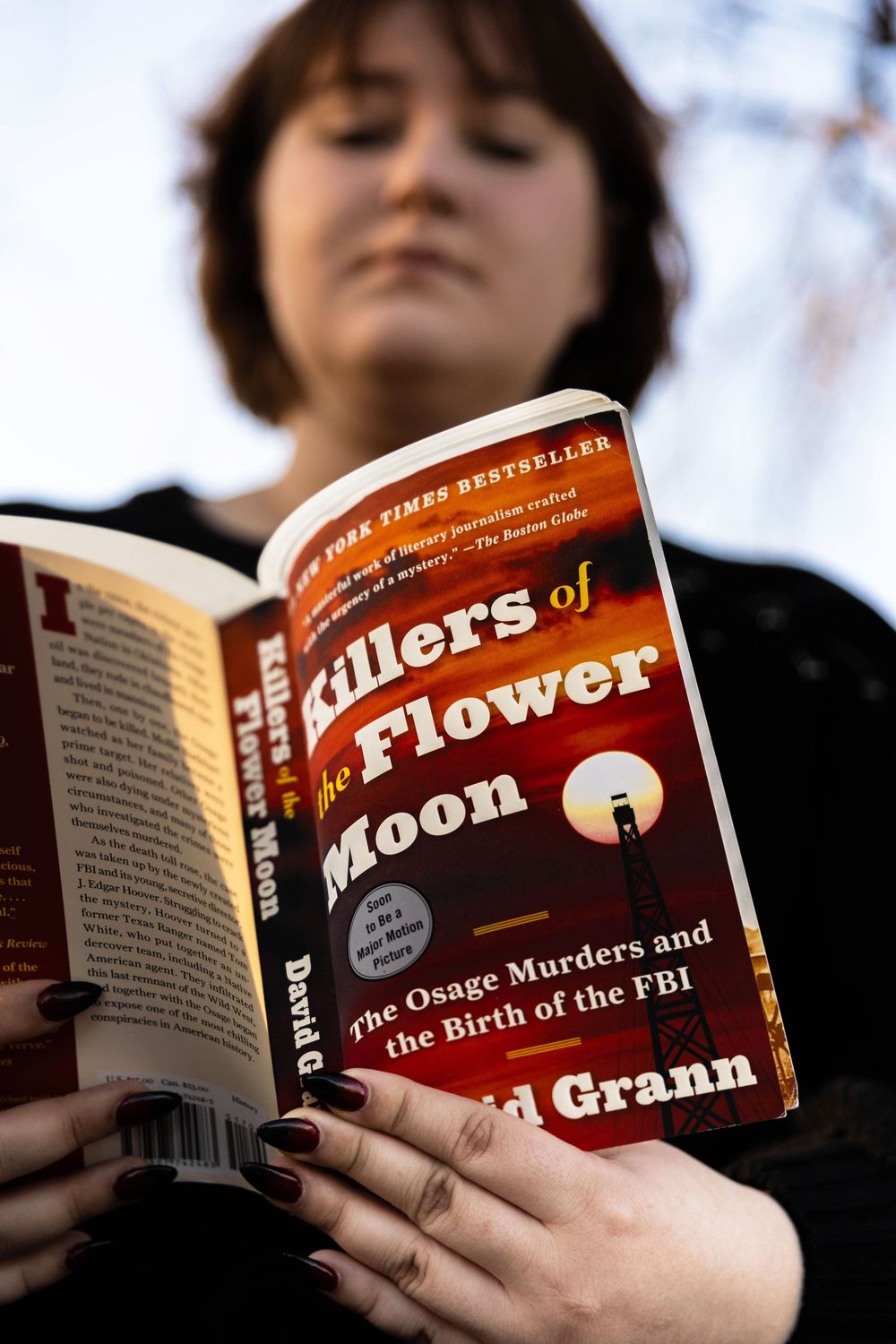 A young girl reading a book titled Killers of the Flower Moon.