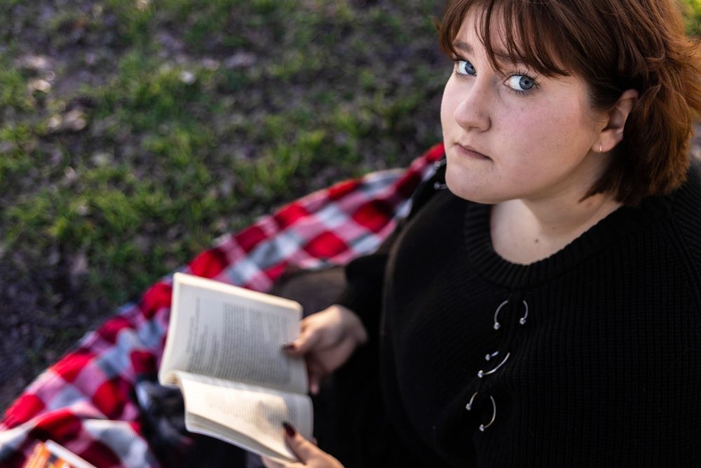 A young girl reading a book on a picnic blanket looks up for a picture.