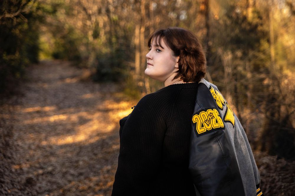 A senior girl poses for her senior photo with her letterman jacket tossed over her shoulder.