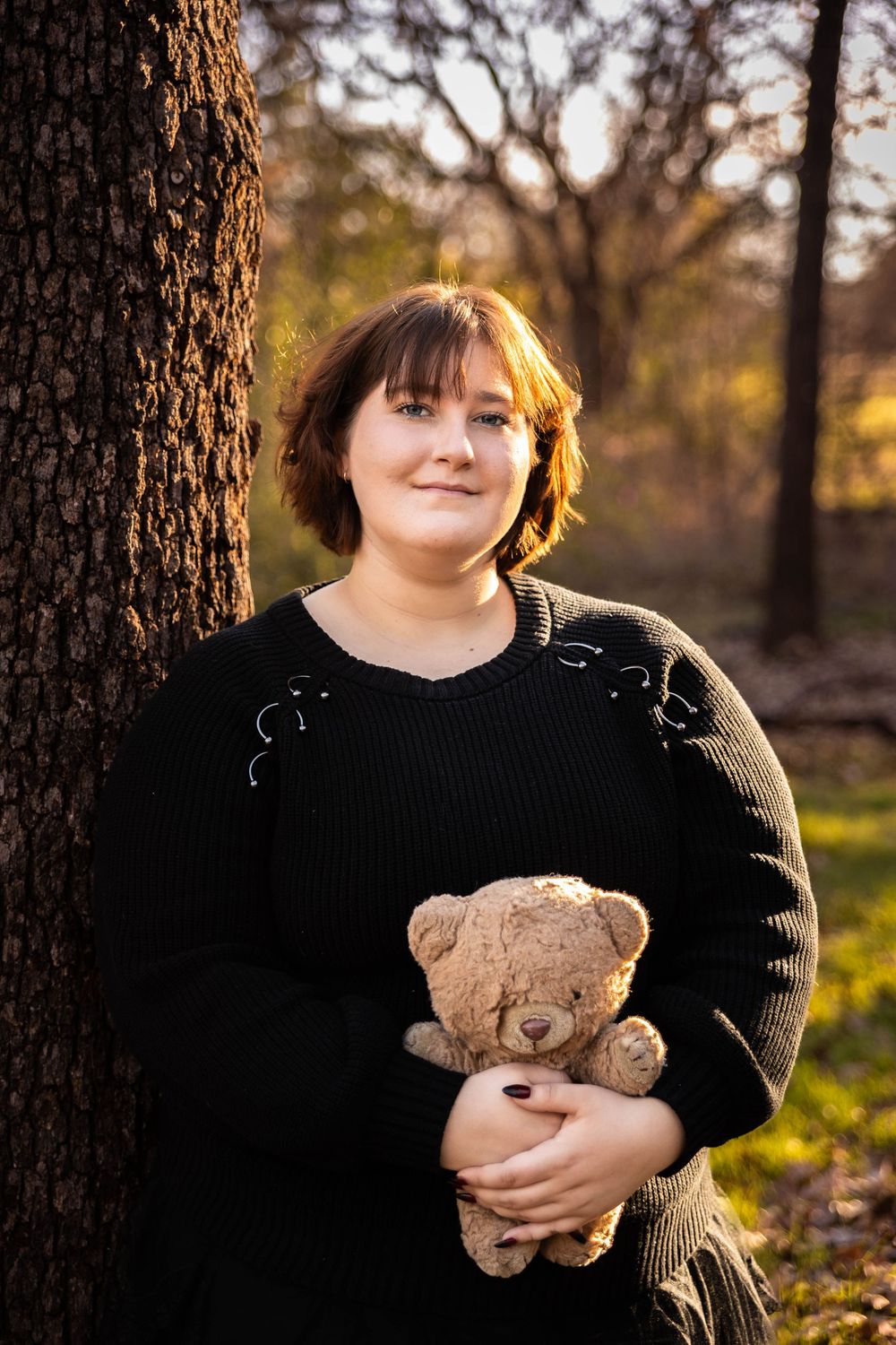 A young girl poses by a tree with a little bear.