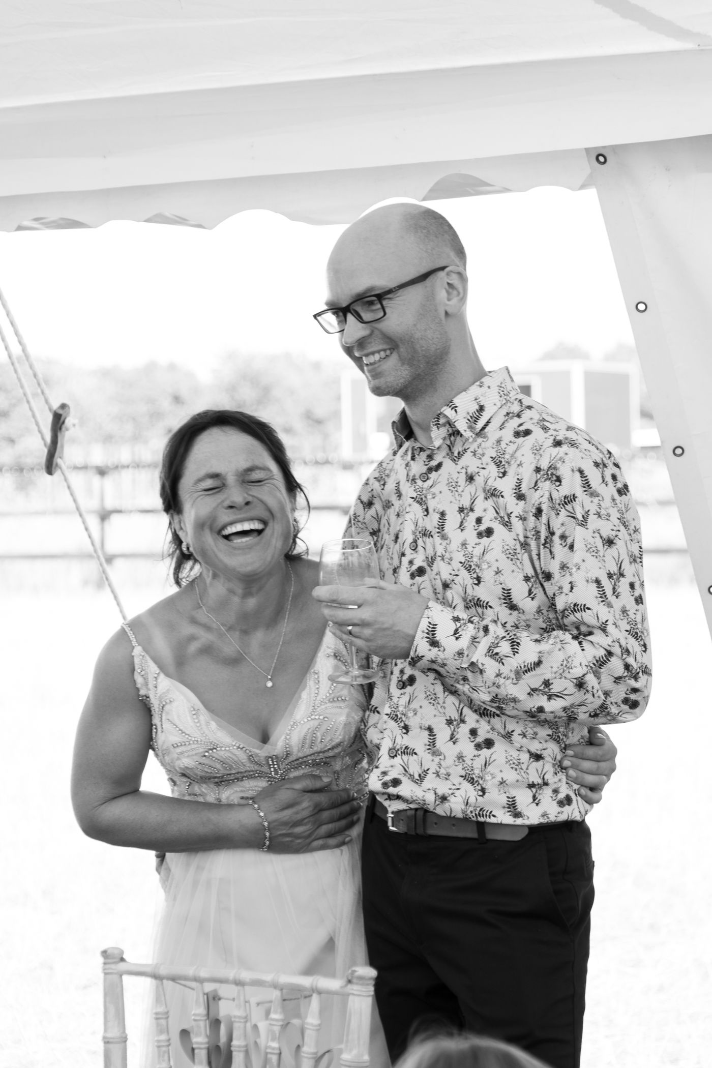 Bride laughing during wedding speeches with groom next to her at their wedding reception