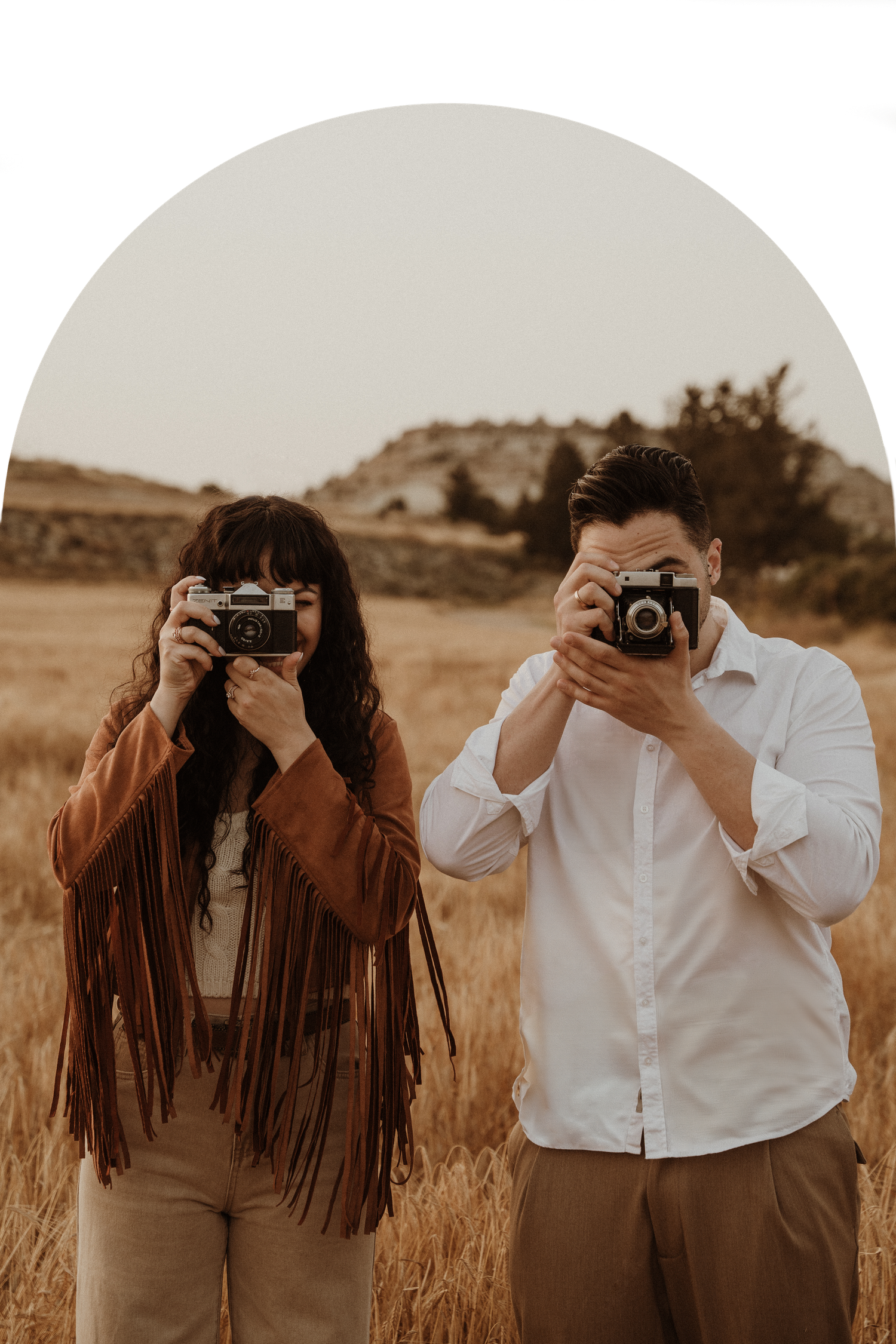 Two photographers stand in a rustic field taking pictures with vintage cameras.