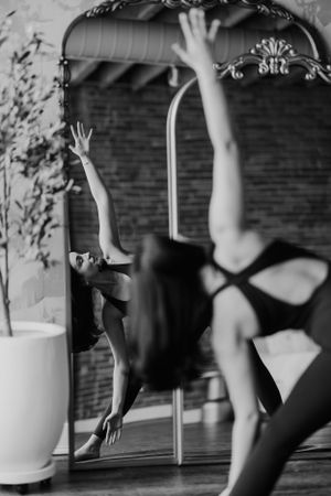 A dancer in black attire performs an elegant movement while being reflected in a large mirror.