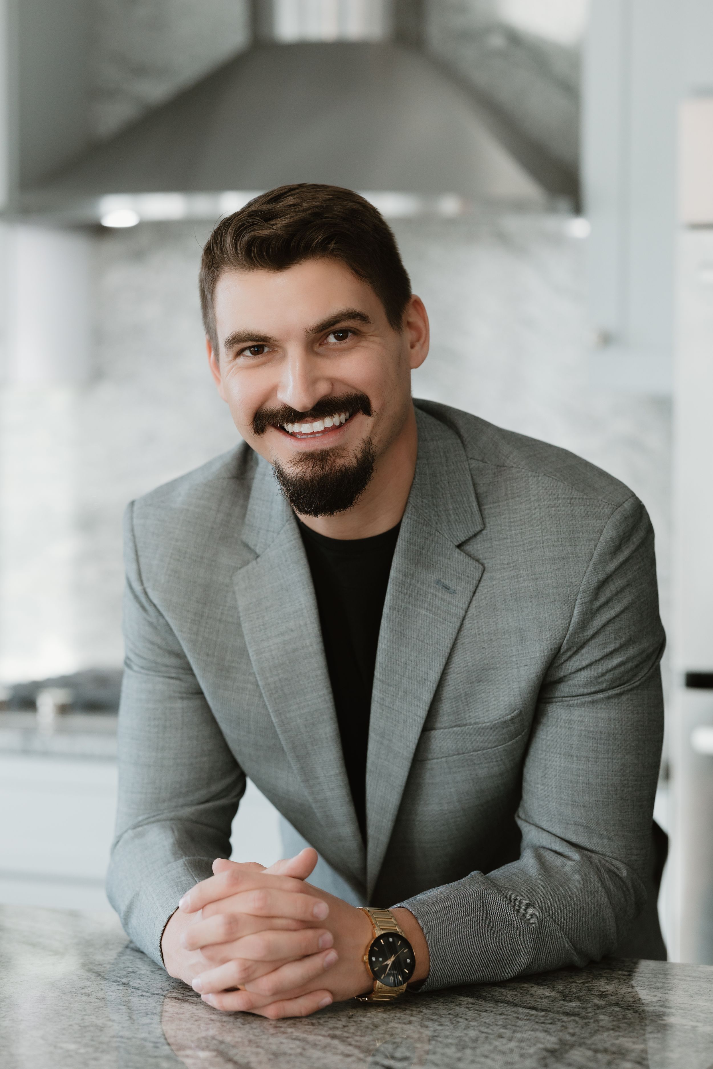 Professional headshot of person in grey blazer smiling at marble counter.