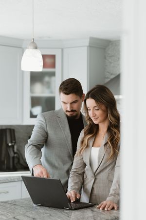 Business professionals collaborating on a laptop at a white marble countertop in a modern office setting.