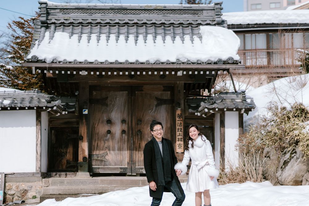 Couple posing in front of a snow-covered traditional Japanese building in winter.