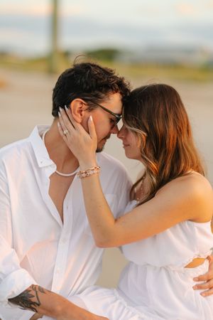 Romantic couple in white shirts share tender moments on the beach at sunset in a series of intimate photographs.
