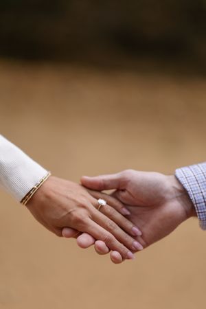 Close-up view of hands holding each other with engagement rings in a romantic moment against a soft blurred background.