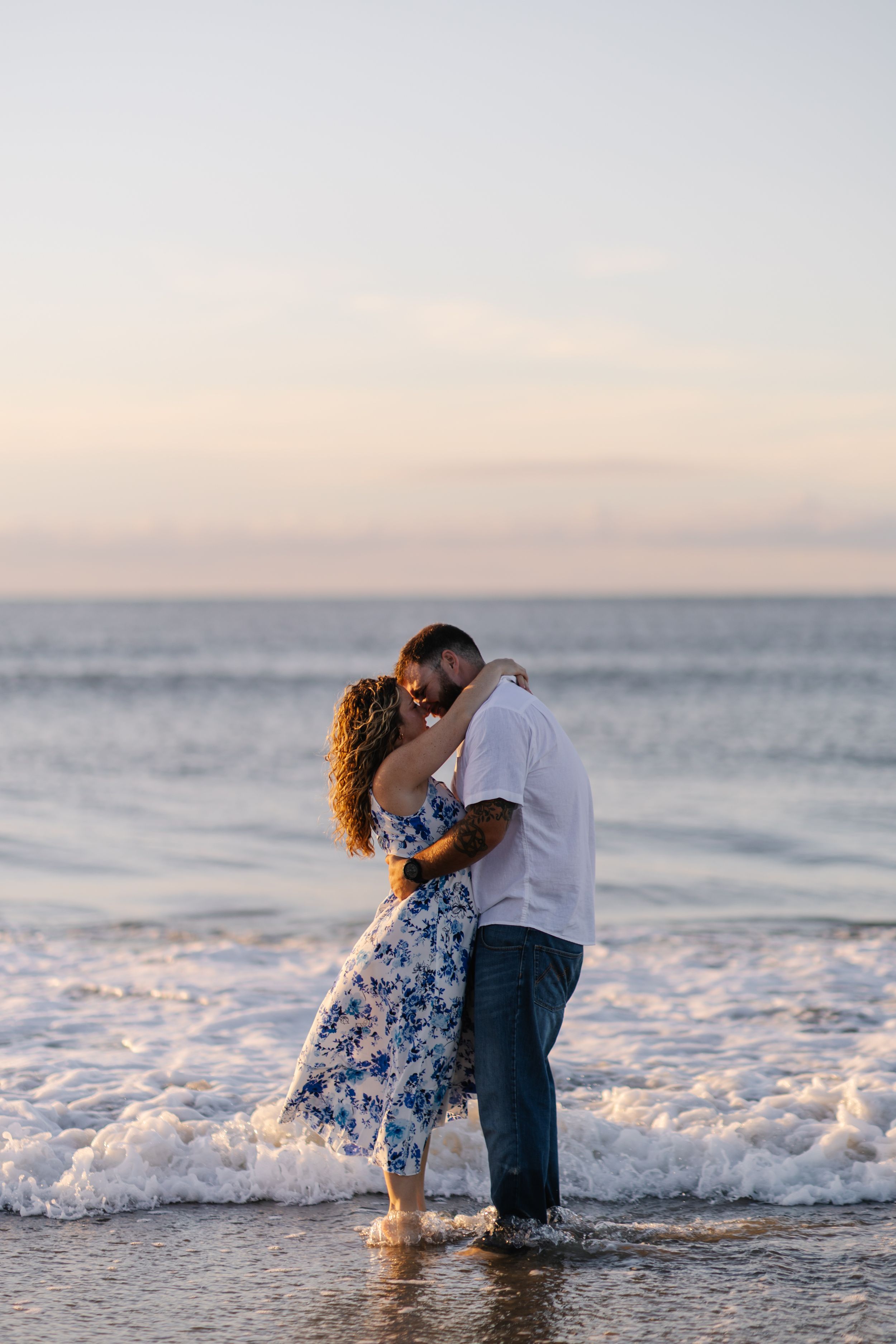 Couple embracing in shallow ocean waves during sunset creating a romantic beach scene.