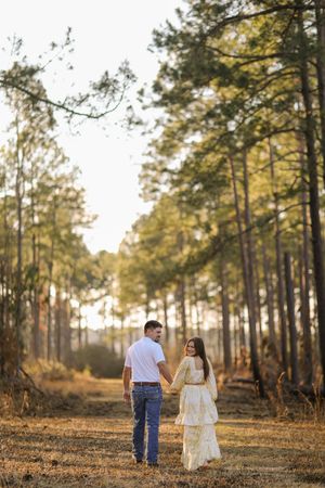 A couple walks hand in hand through a sunlit pine forest during golden hour creating a romantic silhouette.