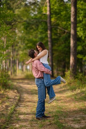 Couple embracing and lifting each other on a tree-lined dirt path in a romantic outdoor photoshoot.