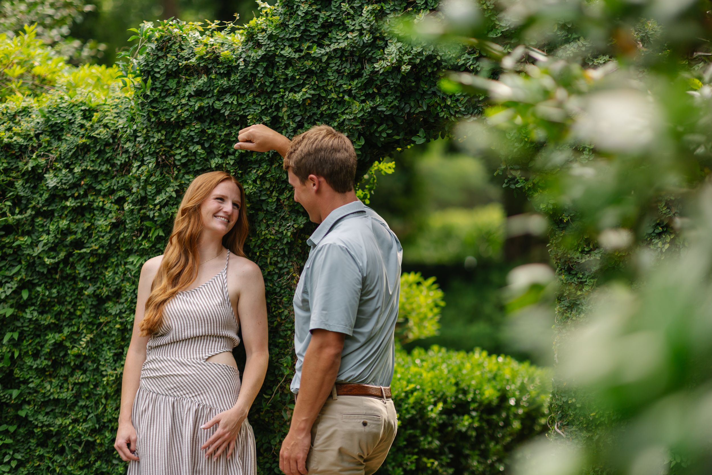 A couple shares a romantic moment surrounded by lush green hedges in a garden setting.