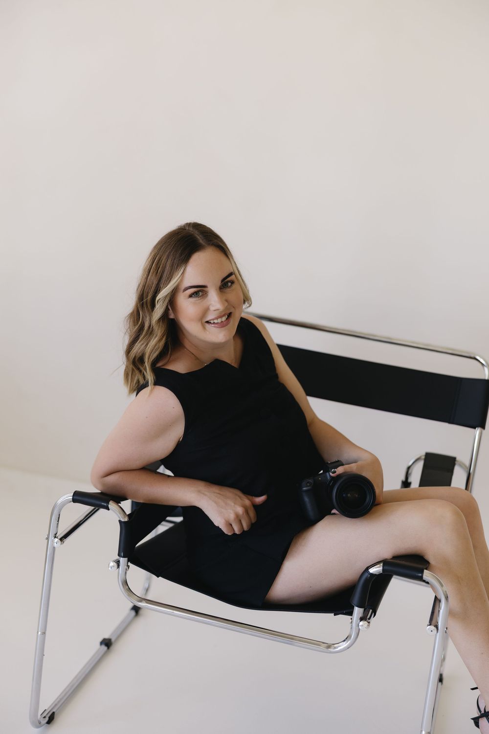 Person in black outfit lounging on a white Wassily chair against neutral background.