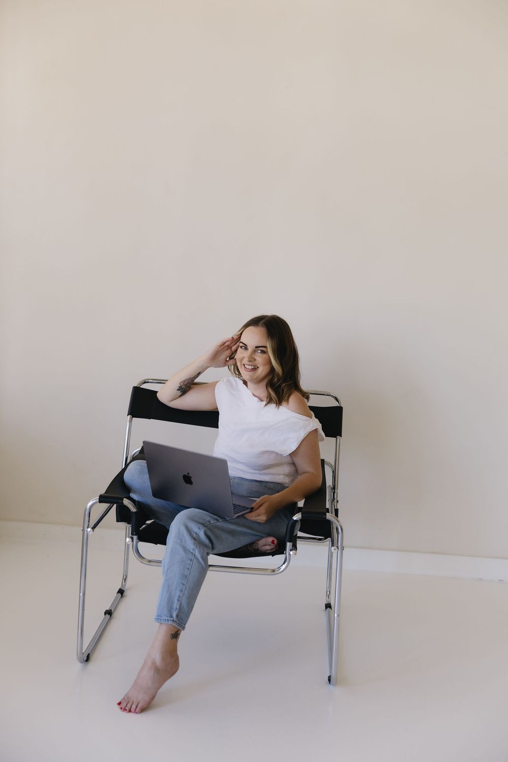 Person in casual attire lounging with laptop on metal bench in minimalist setting.