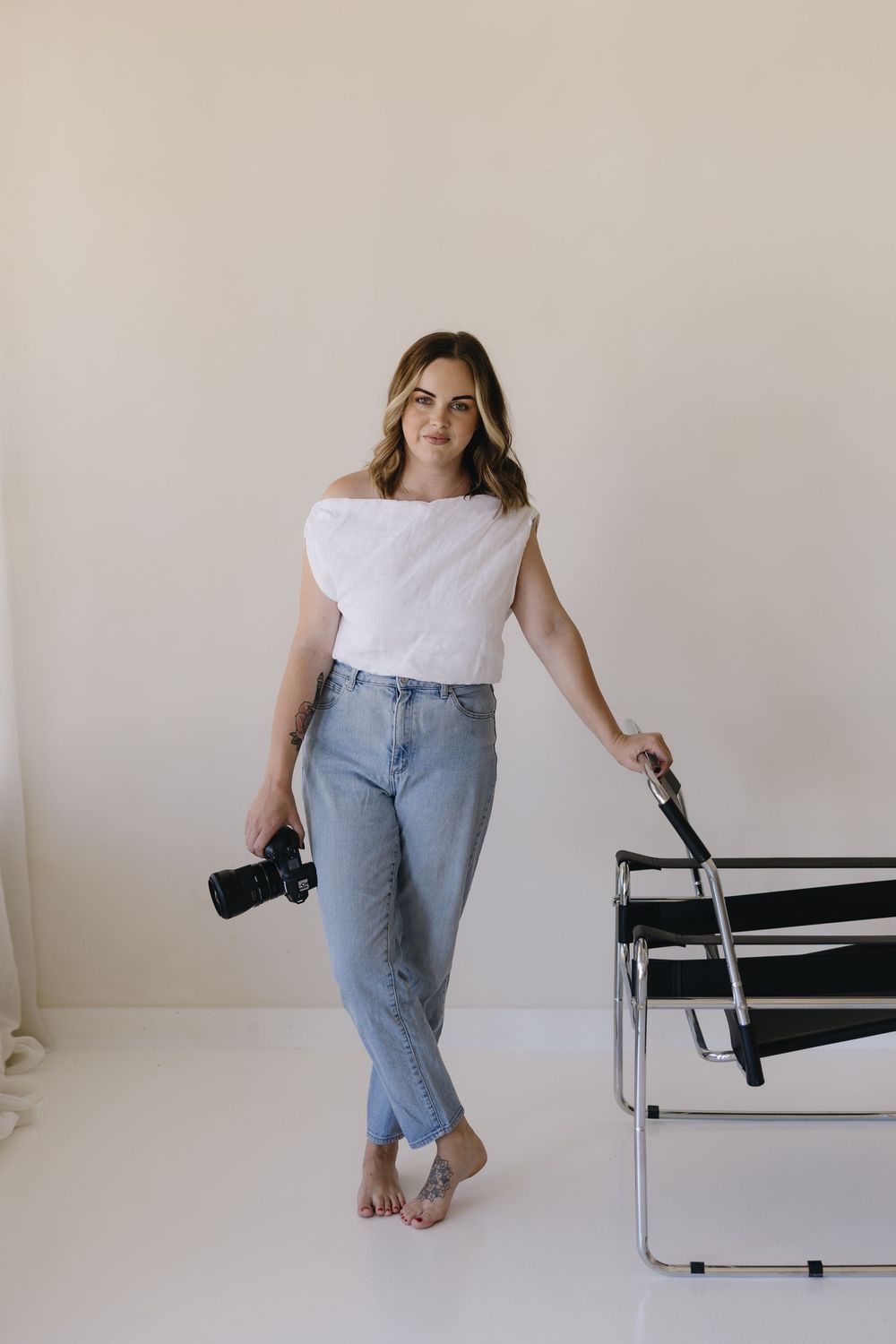 Person in casual white top and jeans posing with camera on modern chrome chair.