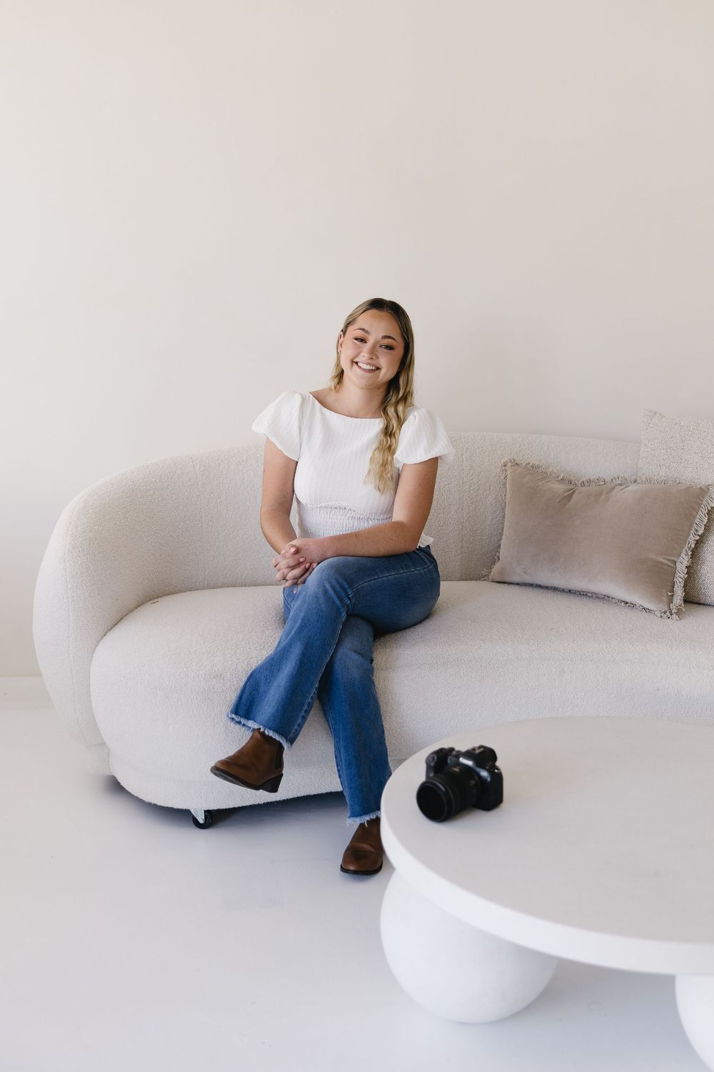 A casual lifestyle photo of someone relaxing on a curved white sofa with a camera on a round coffee table.