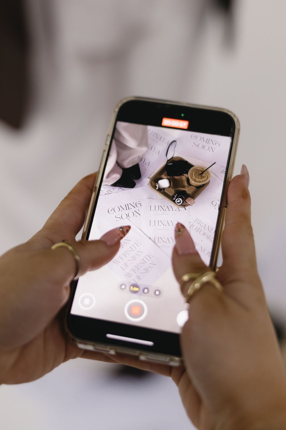 Hands holding smartphone displaying social media app with elegant gold ring accessories.