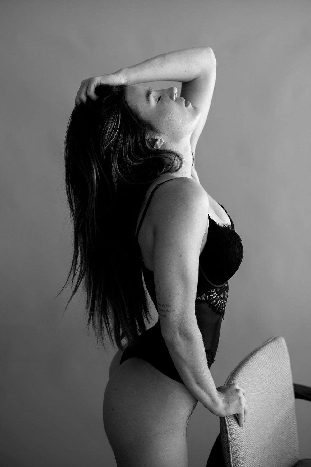 Black and white boudoir photography featuring artistic pose against plain background.
