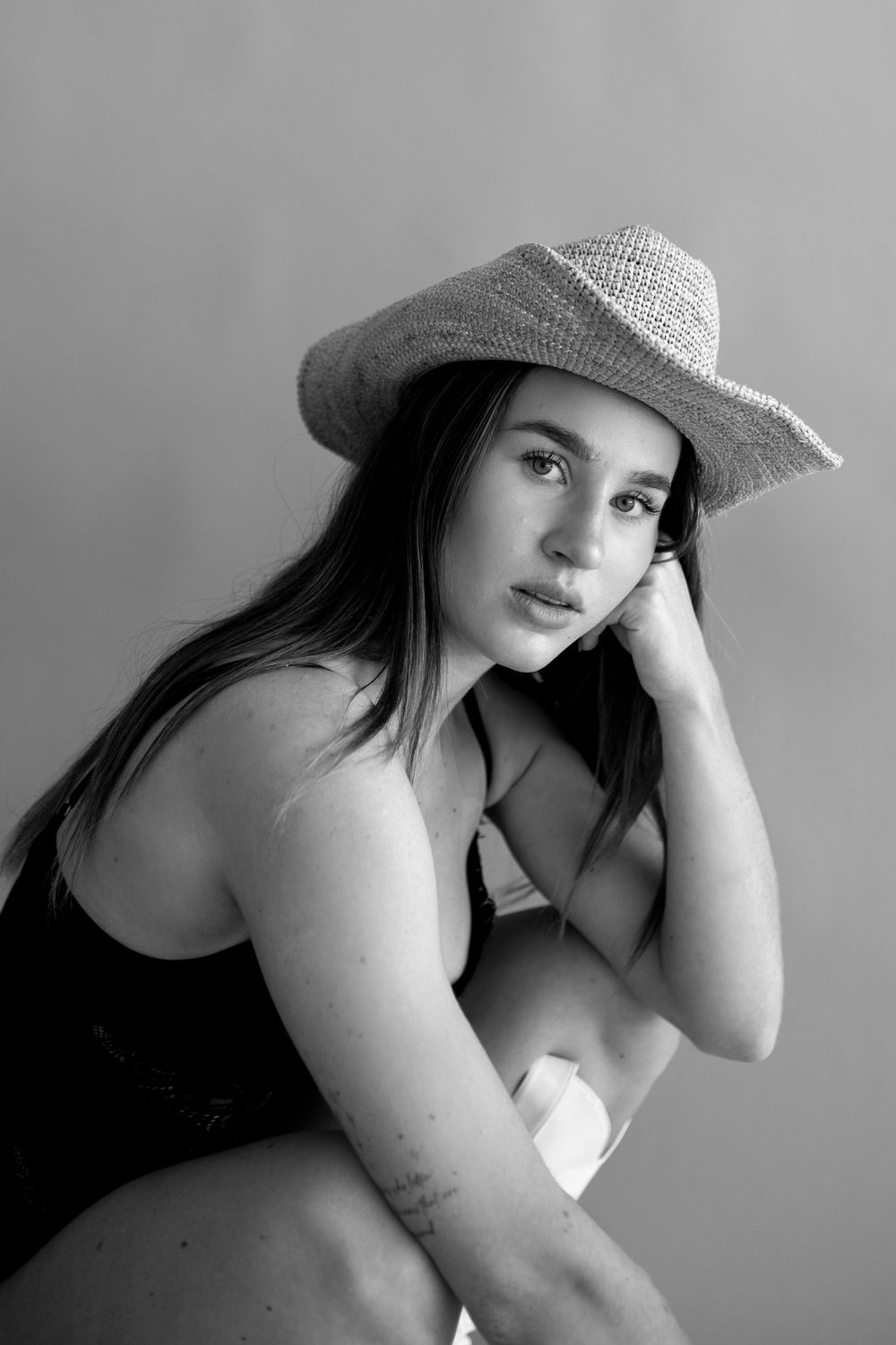 Black and white portrait of person in swimsuit and straw hat in studio setting.