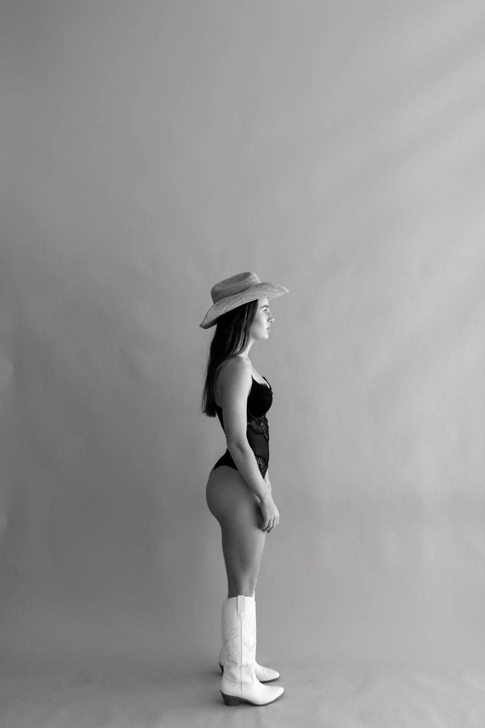 Silhouette in black bodysuit and white boots poses against grey backdrop.